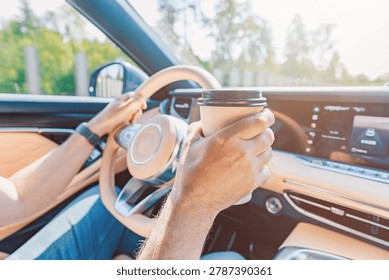 Driver Holds Coffee While Navigating a Modern Car's Dashboard with Sunlight Streaming In
