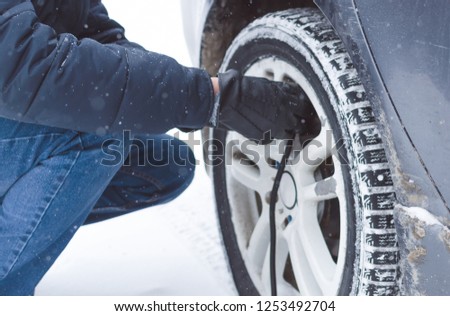 Driver is inflating a tire by car air compressor on the winter road.