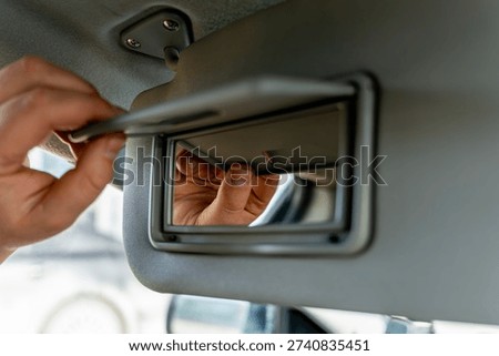 Driver looking at reflection in vanity mirror located in car sun visor, interior close up of vehicle cabin detail.