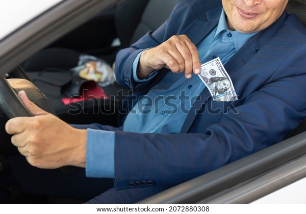 The driver, a man in an\
expensive suit, pulls out 100 dollars from his pocket. The concept\
of bribery on the roads. A deputy gives a bribe to a corrupt\
traffic police