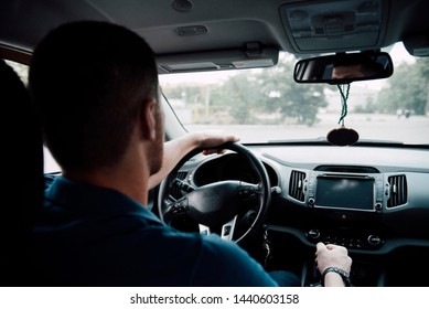 The Driver Man Rides In The Car Behind The Wheel View From The Back Seat. The Driver Behind The Wheel Of The Car.