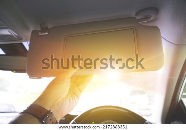 Driver manually adjusting the sun visor in order to\
block sunlight in a car