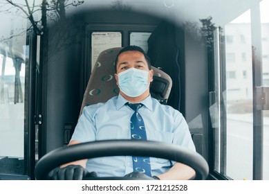 Driver In Mask Looks At Road While Driving. Young Latin Man Bus Driver In Blue Shirt Has Blue Medical Protection Mask And Black  Gloves On Hands.  Bus Driver Wants To Prevent  Infection Of Covid 19.