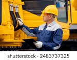 Driver mechanic checks hydraulic hoses of excavator. Man in hard hat industrial worker.