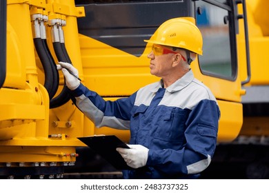 Driver mechanic checks hydraulic hoses of excavator. Man in hard hat industrial worker. - Powered by Shutterstock