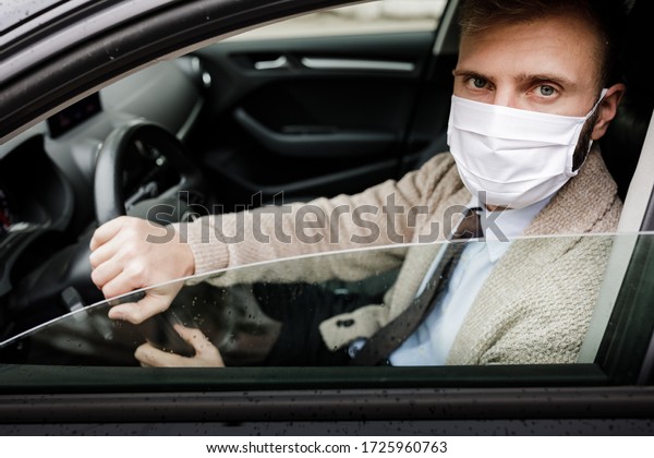 Driver in a medical mask. A man in a car puts on\
a medical mask during an epidemic. Protection from the virus.\
Driver in a jacket in a car. Coronavirus, disease, infection,\
quarantine, covid-19