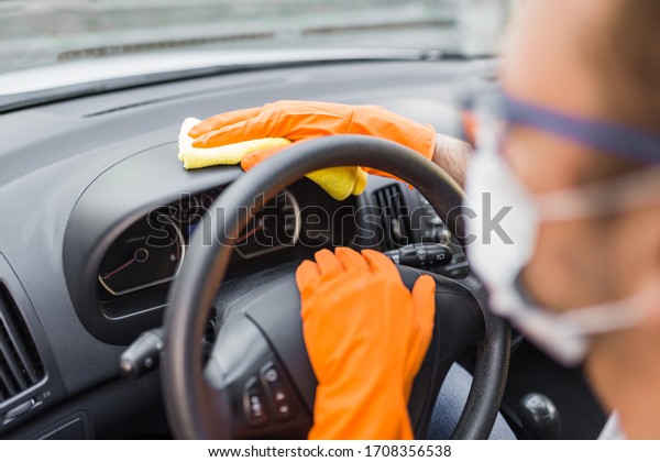 Driver with medical mask and protective\
gloves cleaning car interior with microfiber\
cloth.