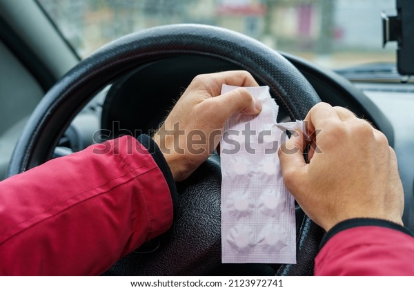 The driver opens a package of pills against a
blurred background of the steering wheel in the car. The use of
pharmacological drugs for medical purposes while driving. Selective
focus, toned