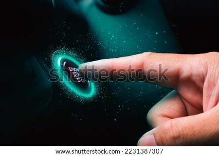 The driver palm as it presses the electric car engine start stop button with a blue light illuminated in the darkness