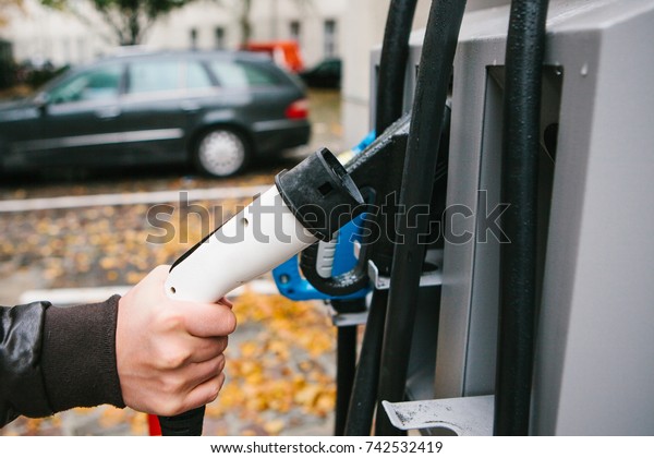 The driver picks up a cable to charge the electric\
vehicle. A modern and eco-friendly mode of transport that has\
spread throughout the\
world.