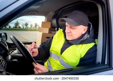 The Driver Plans To Work On The Tablet. Driver Driving A Cargo Van. Satisfied Man At Work. Delivery Of Parcels. The Postman Chooses The Delivery Route. Concept Of Logistics Services.