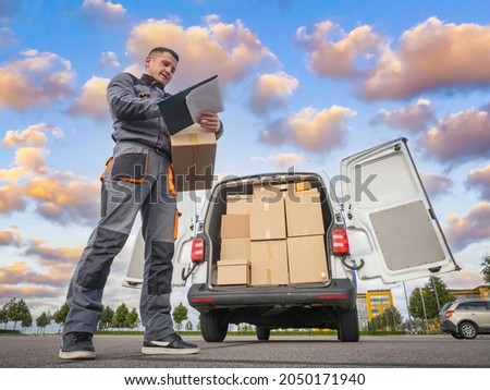 The driver postman draws up documents. Cargo delivery. The van is filled with boxes. Logistics services. The driver unloads a van. The machine is loaded in stock. Mailman at work. Logistics Concept.