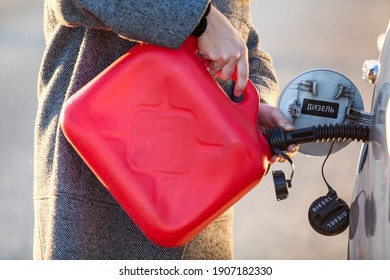 Driver pouring diesel from red plastic oil can into car tank, close up view. Inscription: diesel in Russian on fuel filler flap - Powered by Shutterstock