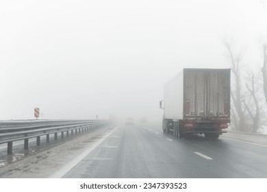 Driver POV on traffic on blue foggy misty rainy slush highway intercity road with low poor visibility on cold winter autumn morning. Seasonal bad rainy weather accident danger warning. car fog light