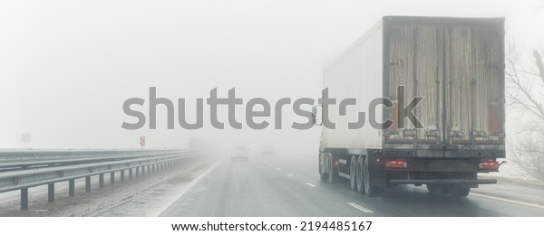 Driver POV on traffic on blue foggy misty rainy\
slush highway intercity road with low poor visibility on cold\
winter autumn morning. Seasonal bad rainy weather accident danger\
warning. car fog light