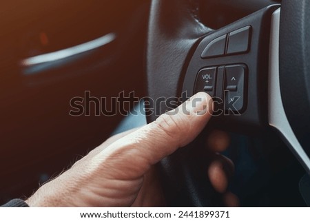 Driver pushing volume down button on car steering wheel, selective focus