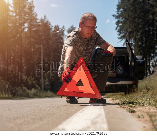 Driver putting red triangle caution sign on road\
near broken auto.