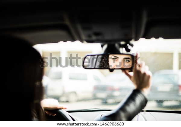 Driver in rear-view mirror. Rear view of attractive\
young woman in casual wear looking in rear-view mirror and smiling\
while driving a car