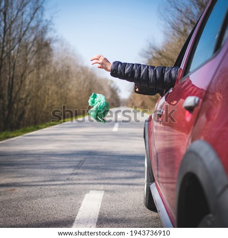 Driver of red car throwing away plastic bag from car window on the road rear view