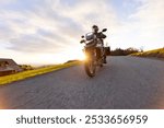 Driver riding motorcycle on empty road during sunset, autumn mountains