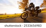 Driver riding motorcycle on empty road during sunset, autumn mountains