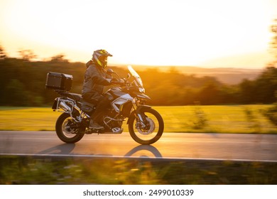 Driver riding motorcycle on empty road during sunset
