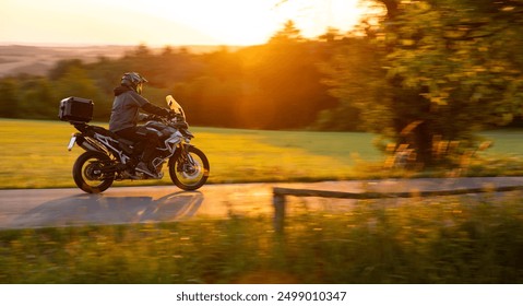 Driver riding motorcycle on empty road during sunset