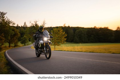 Driver riding motorcycle on empty road during sunset