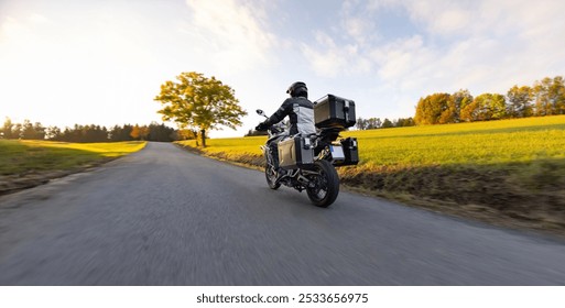 Driver riding motorcycle on empty road during sunset, autumn mountains