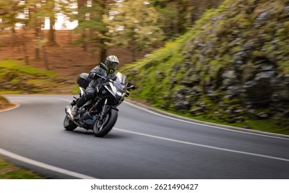 Driver riding motorcycle on empty asphalt road, blurred motiion, spring mountains
