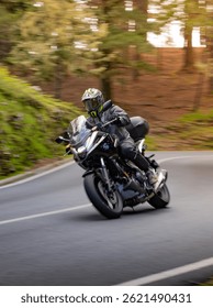 Driver riding motorcycle on empty asphalt road, blurred motiion, spring mountains