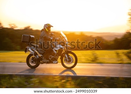 Driver riding motorcycle on empty road during sunset
