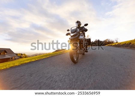 Driver riding motorcycle on empty road during sunset, autumn mountains