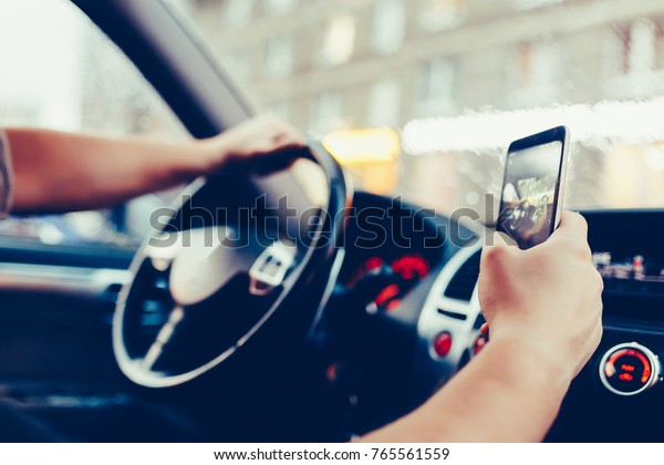 Driver with a smartphone in hand in the driver\'s\
seat. The concept of inattention at the wheel. Distracted by SMS or\
call by mobile. Cropped hand of businessman using phone. Vintage\
style photo