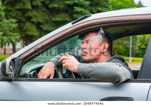 The driver smokes and enjoys a\
cigarette while driving his car, thereby harming his\
health