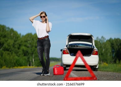 Driver standing with empty fuel canister against car background. Finished fuel. Not enough gasoline. Red emergency triangle stop sign and driver near car background. - Shutterstock ID 2166576699