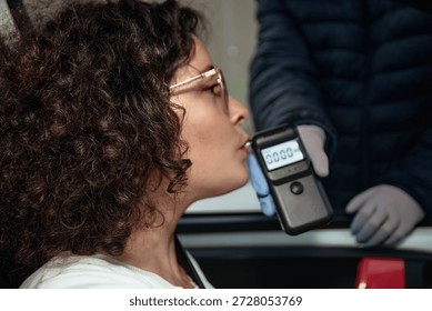 Driver submitting to an alcohol test by blowing into a portable breathalyzer device during a police checkpoint, enforcing drunk driving laws and promoting public road safety