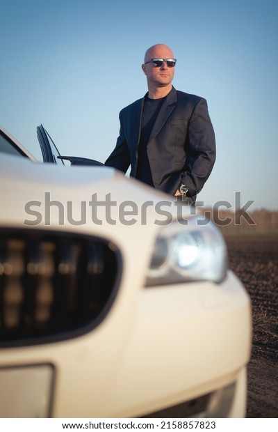 Driver in the suit stands in the field on the empty\
country side road.