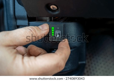 Driver switching LPG fuel system control from petrol to gas inside car, operating onboard alternative fuel selector during vehicle use.