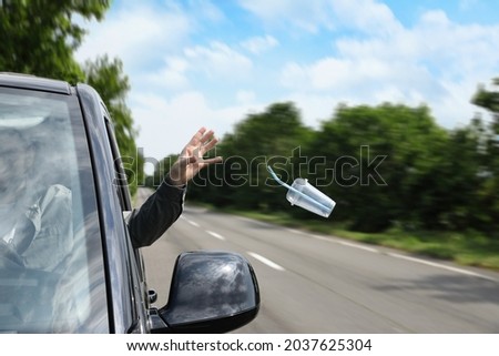 Driver throwing away plastic cup from car window. Garbage on road