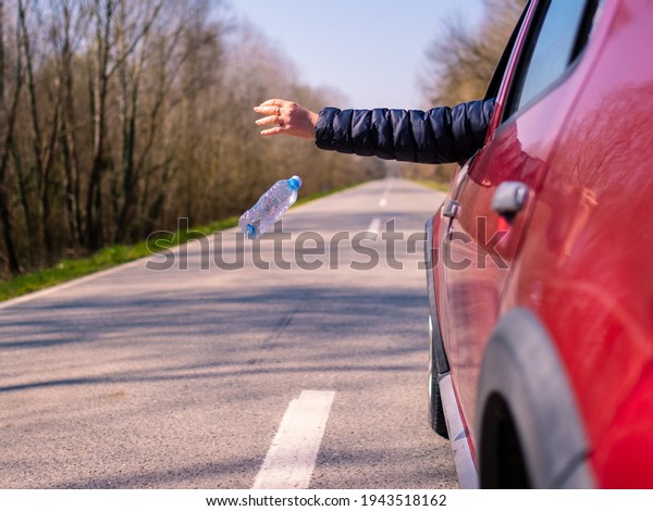 Driver throwing away plastic waste from car window\
on the road rear view