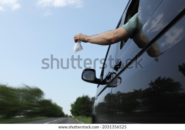 Driver throwing away wet wipe from car window, low\
angle view. Garbage on\
road