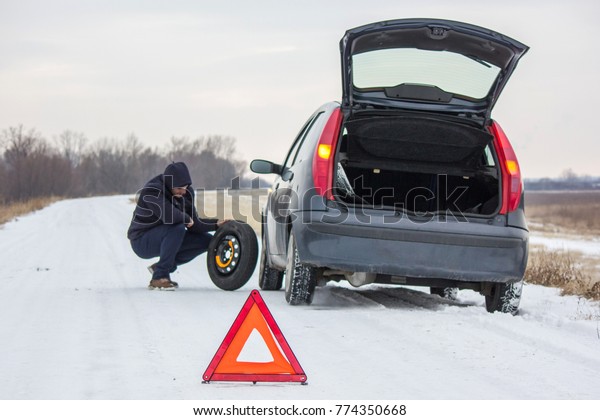 Driver took spare tire to change a flat one on\
winter road