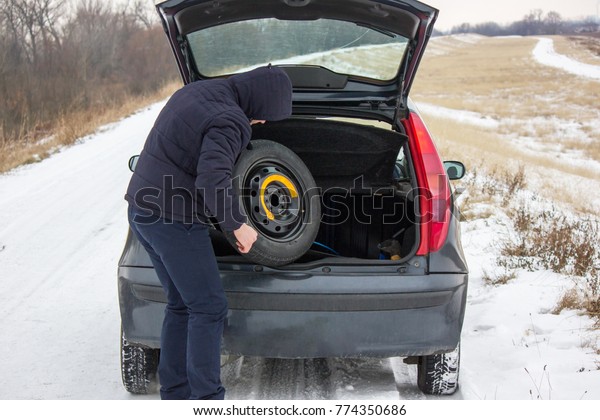 Driver took spare tire from trunk to change a flat\
one on winter road