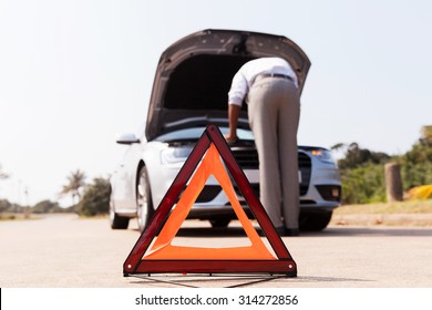 driver trying to figure out how to fix broken down car with red triangle to warn other road users