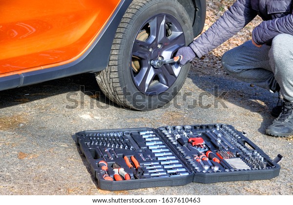 Сar driver using different repair tools for\
repairing a car. Tool set in box near the orange auto. Automobile\
maintenance concept.