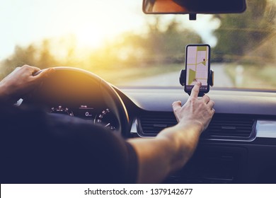 Driver using GPS navigation in mobile phone while driving car at sunset