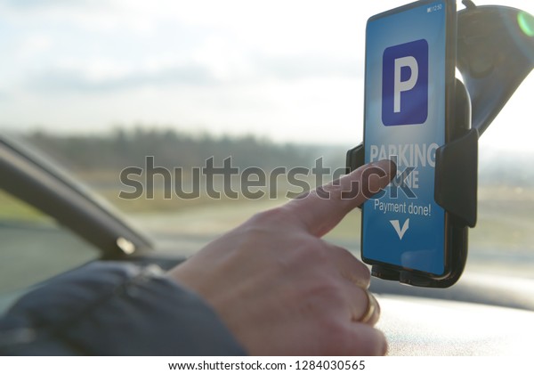 Driver using smartphone app to pay for parking in\
the paid parking zone in a\
city