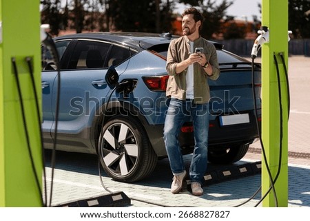Driver using a smartphone while waiting for an electric vehicle to charge at a modern EV charging station, embracing sustainable transportation