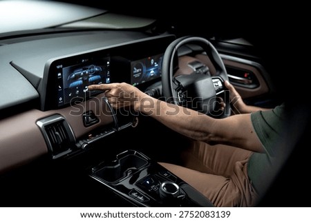 Driver using touchscreen infotainment display inside modern electric vehicle, controlling climate and vehicle functions through digital dashboard interface.
